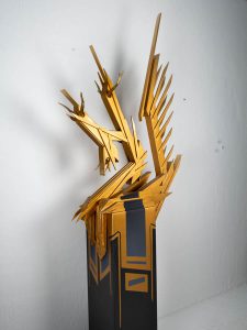 Holzskulptur die Buchstabe Zett darstellt in Gold auf schwarzem sockel