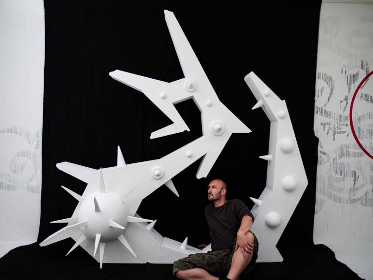 künstler z-rok auf boden sitzend vor einer skulptur aus Styropor, die buchstabe Z darstellt